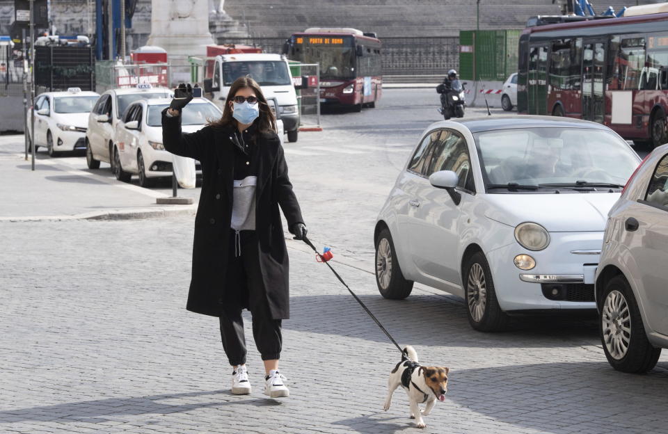 A woman wearing a face mask and gloves walks her dog in Rome, Italy.