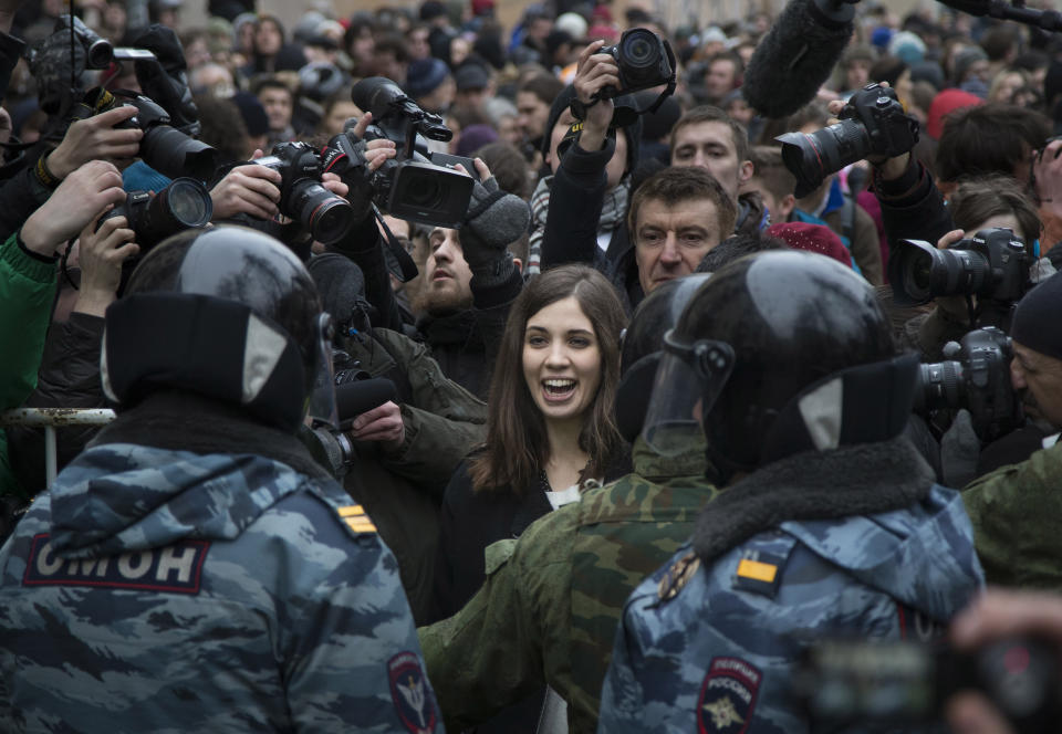 FILE - Nadezhda Tolokonnikova, center, a member of the Pussy Riot punk group, smiles in front of journalists as she stands in front of a police line outside a court in Moscow, Russia, Feb. 24, 2014. Tolokonnikova, who was in prison for nearly 22 months in 2012-13, recalls working 16-18-hour shifts sewing uniforms while at Penal Colony No. 14 in the Mordovia region, (AP Photo/Alexander Zemlianichenko, File)