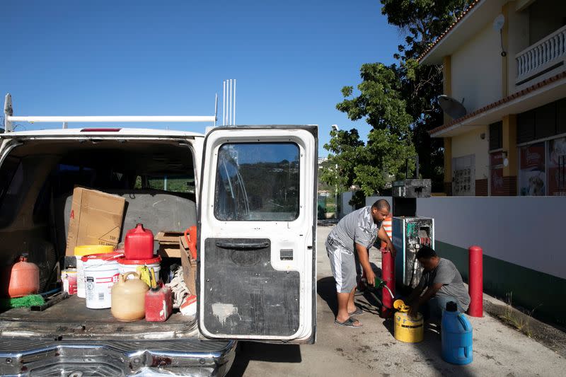 Men fill containers with fuel at a gas station after an earthquake in Guanica