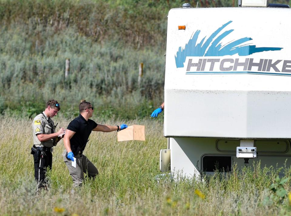 A member of local law enforcement hands a paper bag to someone investigating inside a camper at a crime scene off Highway 38 on Thursday, August 18, 2022, outside of Sioux Falls.