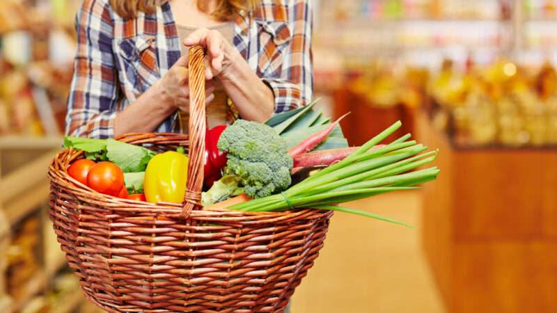 Woman in a supermarket carrying a basket full of fresh produce.