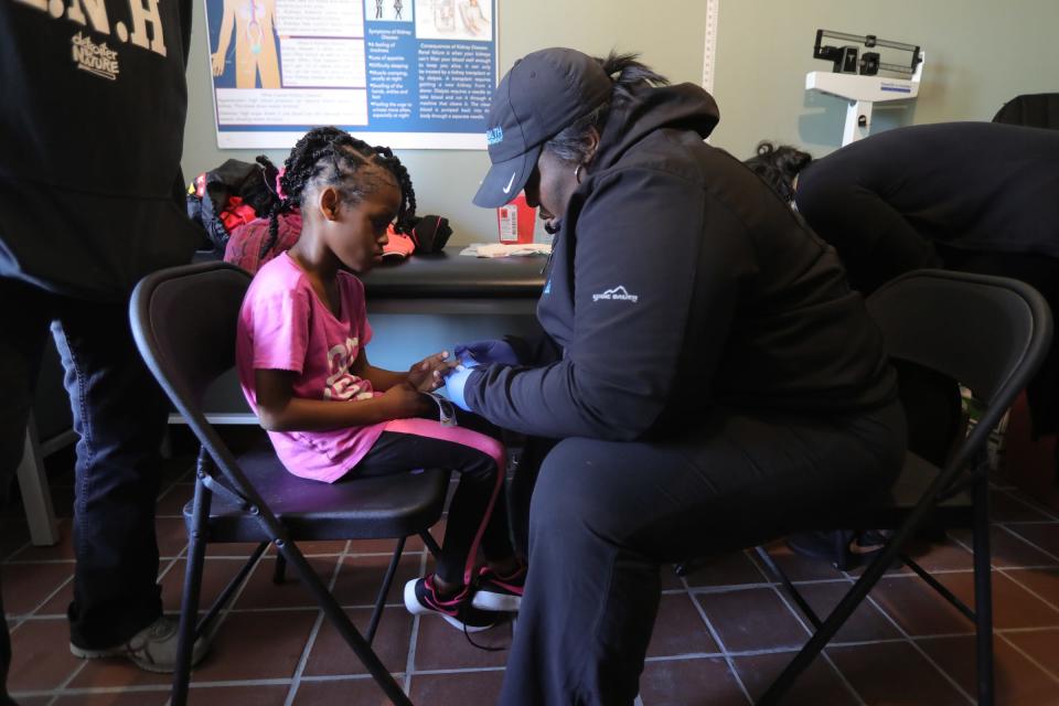 Ashleigh Adams, a city health department employee, tests the lead levels of Lyriq Wilson during a community bazaar put on by Sonia Brown, also known as Auntie Na, on Saturday, Oct. 19, 2019 in Detroit.