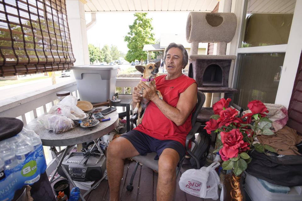 Ben Gallegos sits on the porch of his family's home in the Globeville neighborhood with his dog, Coca Smiles, as the daytime high temperature soars toward triple digits, Thursday, July 27, 2023, in north Denver. Gallegos has taken several measures to keep his home cool in spite of lacking central air conditioning. (AP Photo/David Zalubowski)