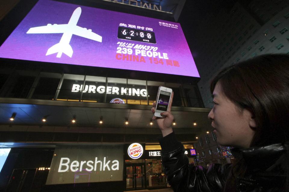 FILE - This March 10, 2014 file photo shows a woman taking a photo of a screen displaying the number of hours since a Malaysia Airlines passenger jet had gone missing at a mall in Beijing, China. For nearly five years, government and industry officials have been exploring a variety ways to make it easier to find airliners and their critical “black boxes” when they end up in the ocean, but the effort was too late to help in the case of a Malaysia Airlines jet that disappeared over the weekend. (AP Photo, File) CHINA OUT