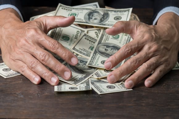 Businessman pulling pile of $100 bills off a table