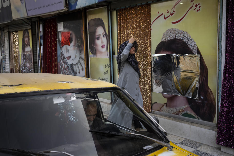 An Afghan woman walks past beauty salons with defaced window decorations, in Kabul, Afghanistan, Sunday, Sept. 12, 2021. Since the Taliban gained control of Kabul, several images depicting women outside beauty salons have been removed or covered up. (AP Photo/Bernat Armangue)