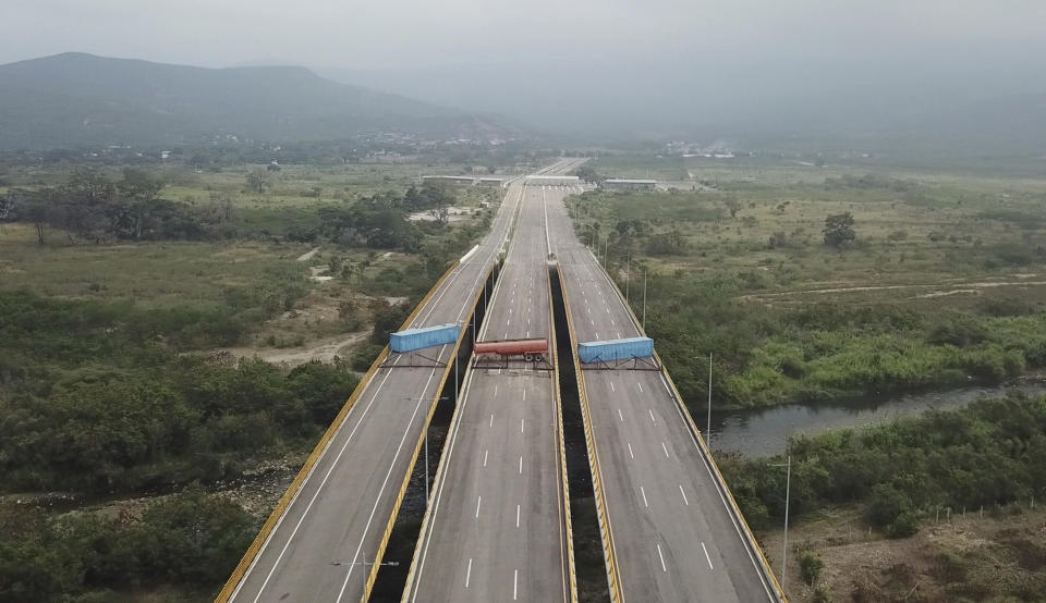 This image taken from video, shows a fuel tanker, cargo trailers and makeshift fencing, blocking the Tienditas International Bridge in an attempt to stop humanitarian aid entering from Colombia, as seen from the outskirts of Cucuta, on Colombia's border with Venezuela, Wednesday, Feb. 6, 2019. Immigration authorities say the Venezuelan National Guard built the roadblock a day earlier. (AP Photo)