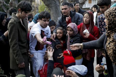 A volunteer (2nd L) gives away goods to stranded refugees and migrants, most of them Afghans, who find shelter on Victoria Square in Athens, Greece, March 3, 2016. REUTERS/Alkis Konstantinidis