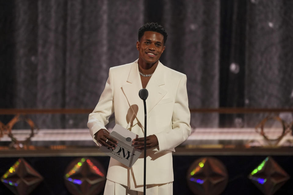 Jeremy onstage smiling in front of a microphone and holding an envelope