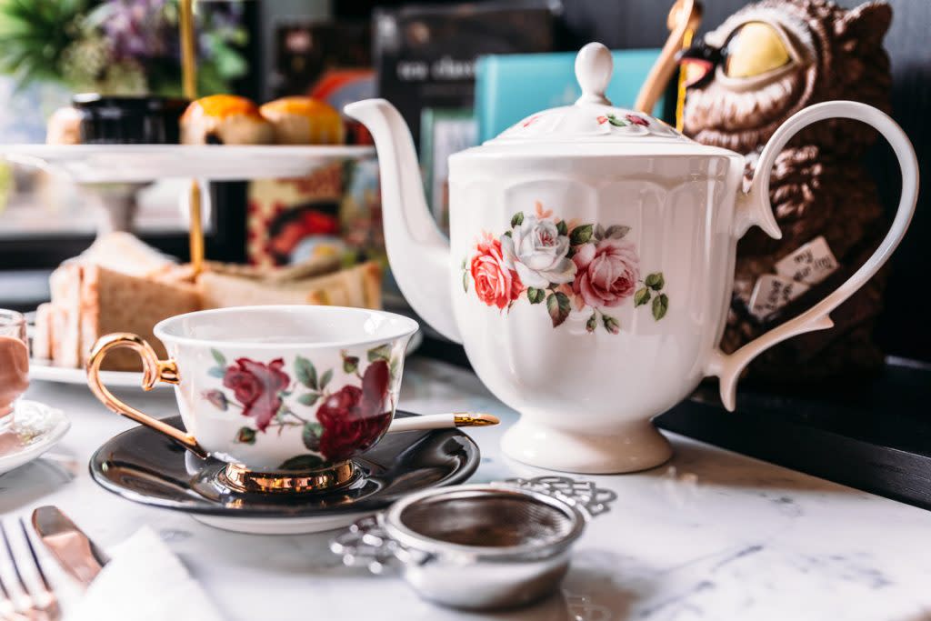 An antique teapot sits on a table with antique tea cups. 