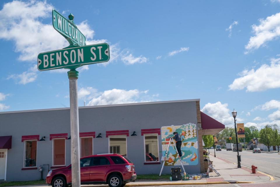 Rhiannan Sibbald, 28, of Greenville, works on a mural near the intersection of Wilcox Avenue and Benson Street in White Cloud on Wednesday, May 8, 2024.