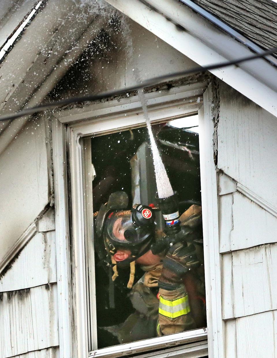 A Rochester firefighter directs water to the roofline from inside the third story floor at 114 Green St. in Somersworth Monday, Oct. 3, 2022.