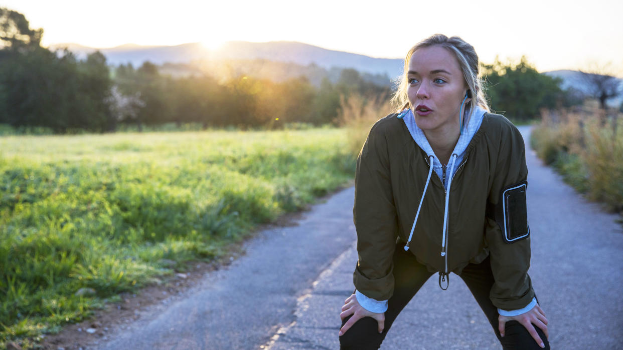  Young woman outdoors, taking a break from exercising, hands on knees. 