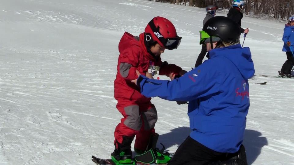 A Sugarbush instructor helps a child onto a snowboard on Feb. 12, 2023. Sugarbush is owned by Alterra Mountain Company.