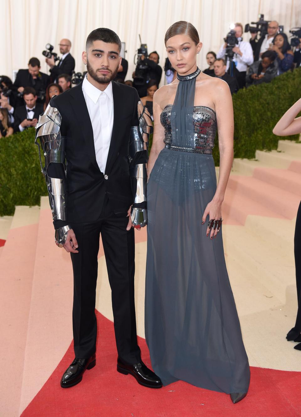 Zayn Malik at the 2016 Met Gala wearing a suit with metal armor on the arms with gigi hadid next to him in a blue gown