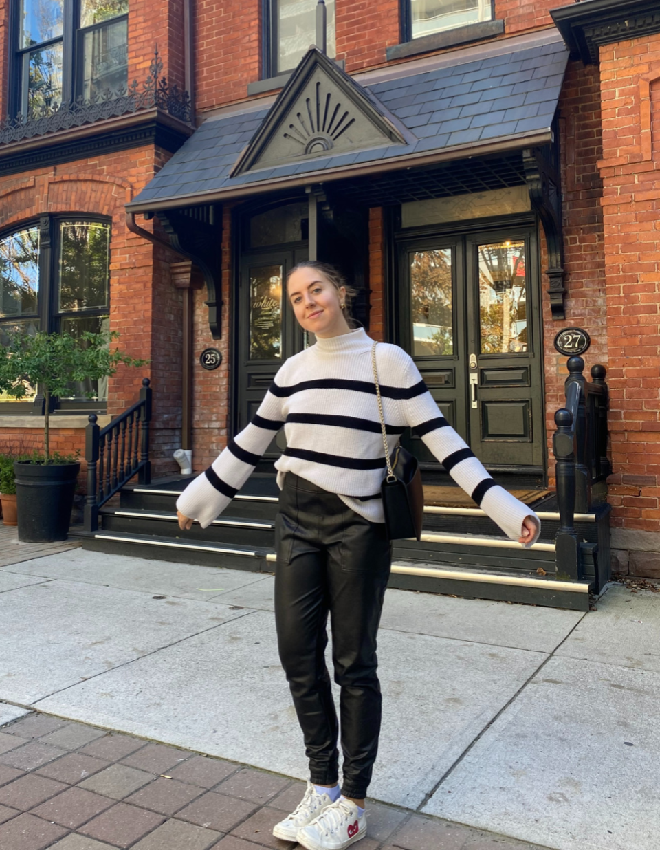 brunette woman in striped black and white sweater and black leather spanx pants and converse sneakers outside