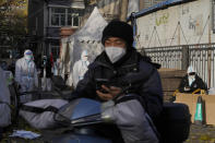 A delivery man passes by workers in protective clothing controlling access into a community under lockdown in Beijing, Friday, Nov. 25, 2022. Residents of China's capital were emptying supermarket shelves and overwhelming delivery apps Friday as the city government ordered accelerated construction of COVID-19 quarantine centers and field hospitals. (AP Photo/Ng Han Guan)