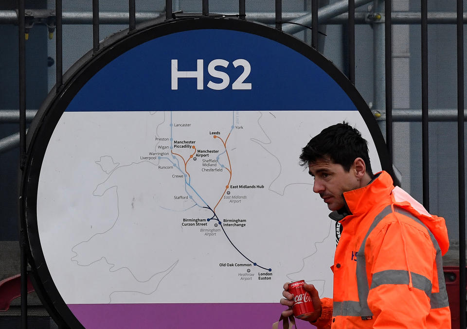 An HS2 worker walks past signage on perimeter fencing at the HS2 high speed rail link construction site in Euston, London, Britain, December 18, 2019. REUTERS/Toby Melville