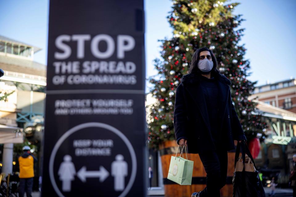 Pedestrians wearing a protective face covering to combat the spread of the coronavirus, pass a COVID-19 information sign reading "STOP the spread" as they walk past a Christmas tree in Covent Garden in central London, on November 22, 2020, as the four-week national shutdown imposed in England continues, forcing people to stay home and businesses to close owing to a second wave of the Covid-19 pandemic. - British Prime Minister Boris Johnson will confirm that coronavirus lockdown restrictions across England are to end on December 2, his office said Saturday. The lockdown will be followed by a return to a three-tiered set of regional restrictions as part of the government's "COVID Winter Plan", it added in a statement. (Photo by Tolga Akmen / AFP) (Photo by TOLGA AKMEN/AFP via Getty Images)