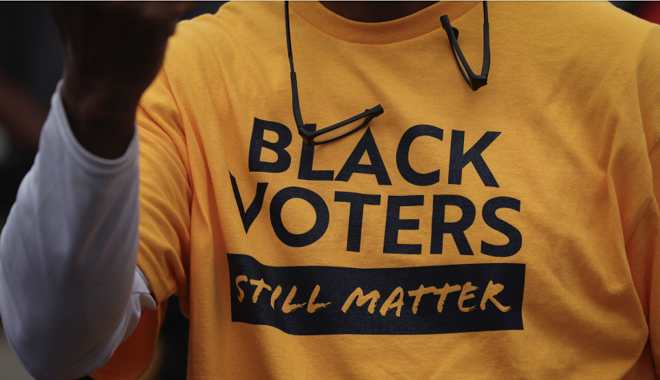 Person wearing a shirt with the text "Black Voters Still Matter" and sunglasses hanging from the collar