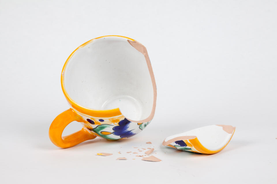 A broken ceramic mug with a large piece detached, leaving fragments. The mug's design includes floral patterns