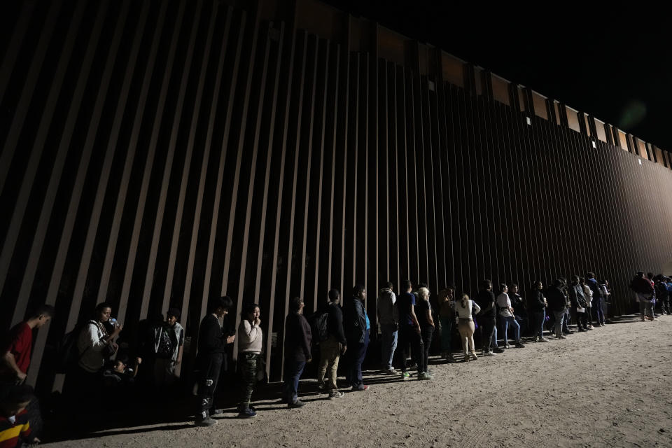 People line up against a border wall as they wait to apply for asylum after crossing the border from Mexico Tuesday, July 11, 2023, near Yuma, Arizona. Thousands of migrants from the north African country of Mauritania have arrived in the U.S. in recent months, following a new route taking them to Nicaragua and up through the southern border. (AP Photo/Gregory Bull)