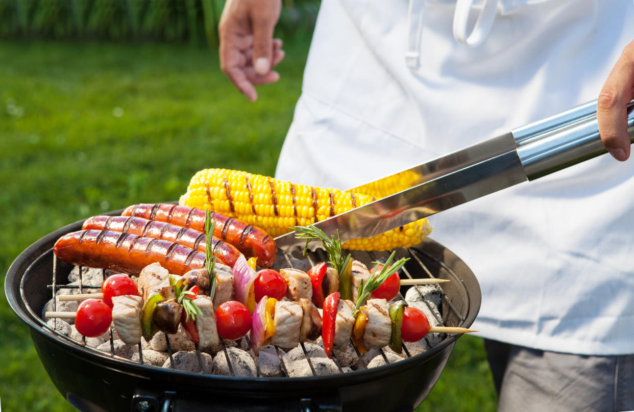 Man with tongs cooking on a back yard barbecue.