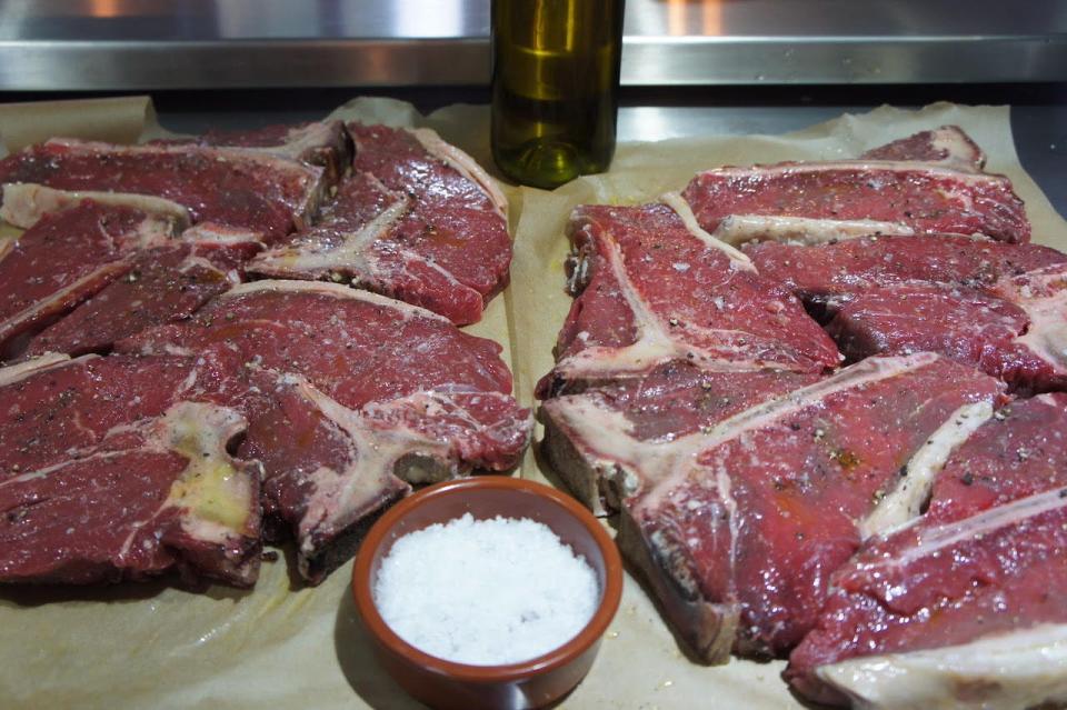 Raw steaks covered in salt with a bowl of salt between them