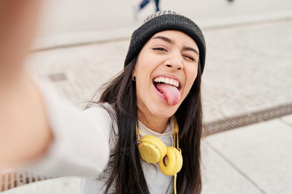 latina taking a selfie with her smart phone sticking out her tongue and winking hispanic woman making a funny face while taking a selfie