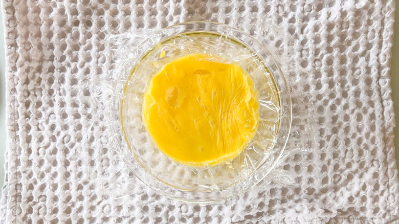 Lemon curd in bowl covered with plastic wrap over towel