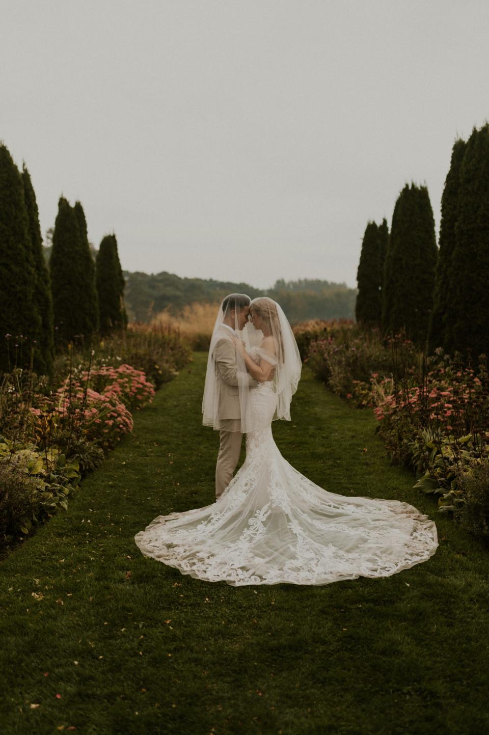 A bride and groom embrace under her veil in a garden.