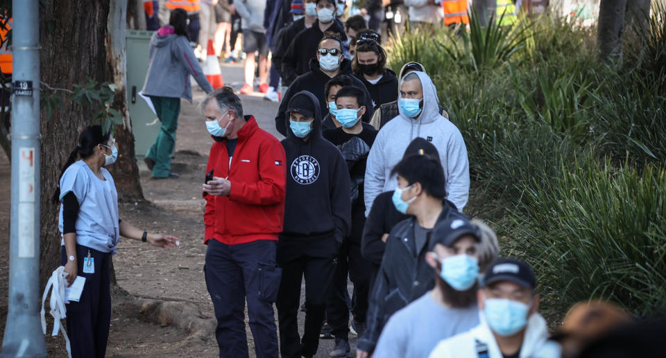 Tradesmen and women stand in a line wearing face masks as they wait to be vaccinated at the Sydney Olympic Park Vaccination Centre at Homebush in Sydney, Sunday, August 15, 2021. Source: AAP