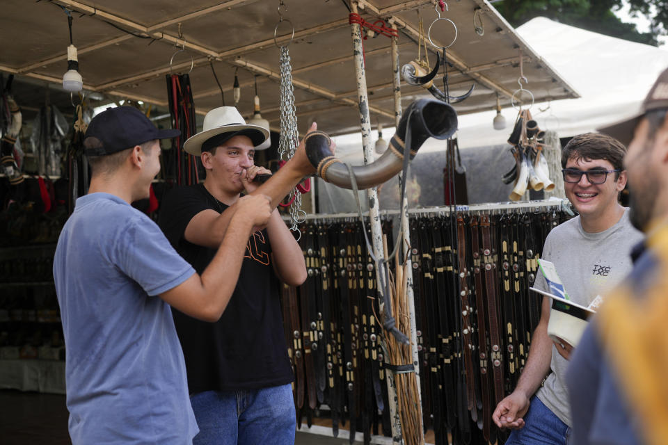 A youth blows into a horn at a vendor's stall at the ExpoZebu fair in Uberaba, Minas Gerais state, Saturday, April 27, 2024. Uberaba holds an annual gathering called ExpoZebu that bills itself as the world’s biggest Zebu fair. (AP Photo/Silvia Izquierdo)