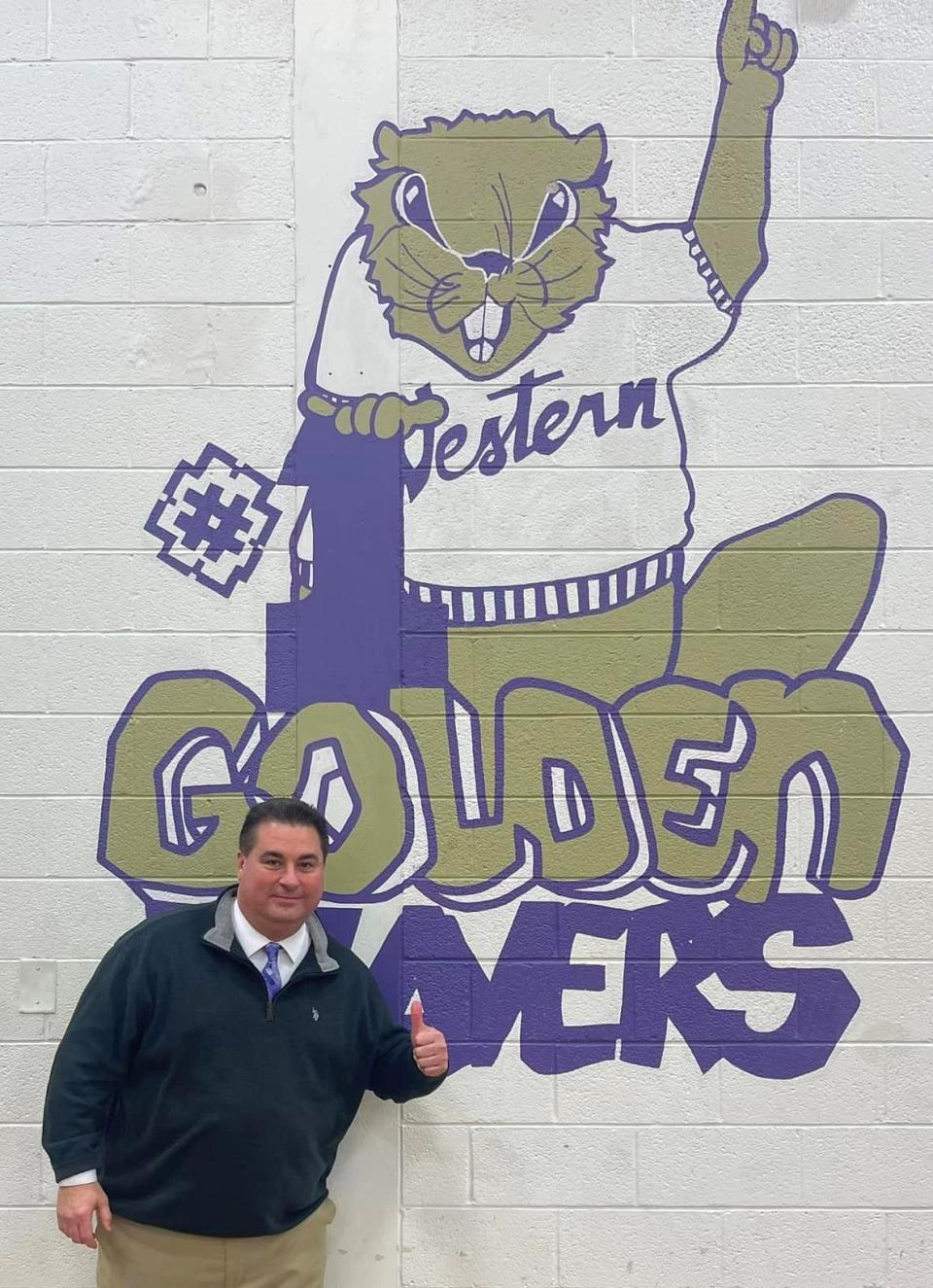 John Rosa poses before the Western Beaver logo at the high school last Wednesday night after he was hired as the Golden Beavers' athletic director.