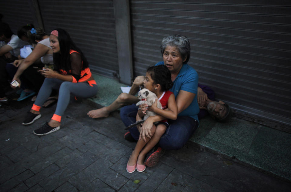 Maryeli Verde holds her niece Yalin, who clutches her cat Will, as Yalin's grandfather Tonisio, who is sick, lies behind them after they evacuated their apartment on the ninth floor after a powerful earthquake shook eastern Venezuela, causing buildings to be evacuated in the capital of Caracas, Venezuela, Tuesday, Aug. 21, 2018. The quake was felt as far away as Colombia's capital and in the Venezuelan capital office workers evacuated buildings and people fled homes. (AP Photo/Ariana Cubillos)