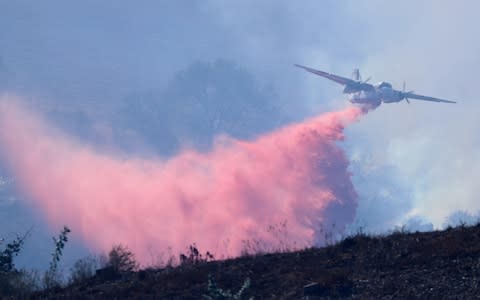 A plane dumps flame retardant on a fast moving fire in Bonsall, California - Credit: Reuters