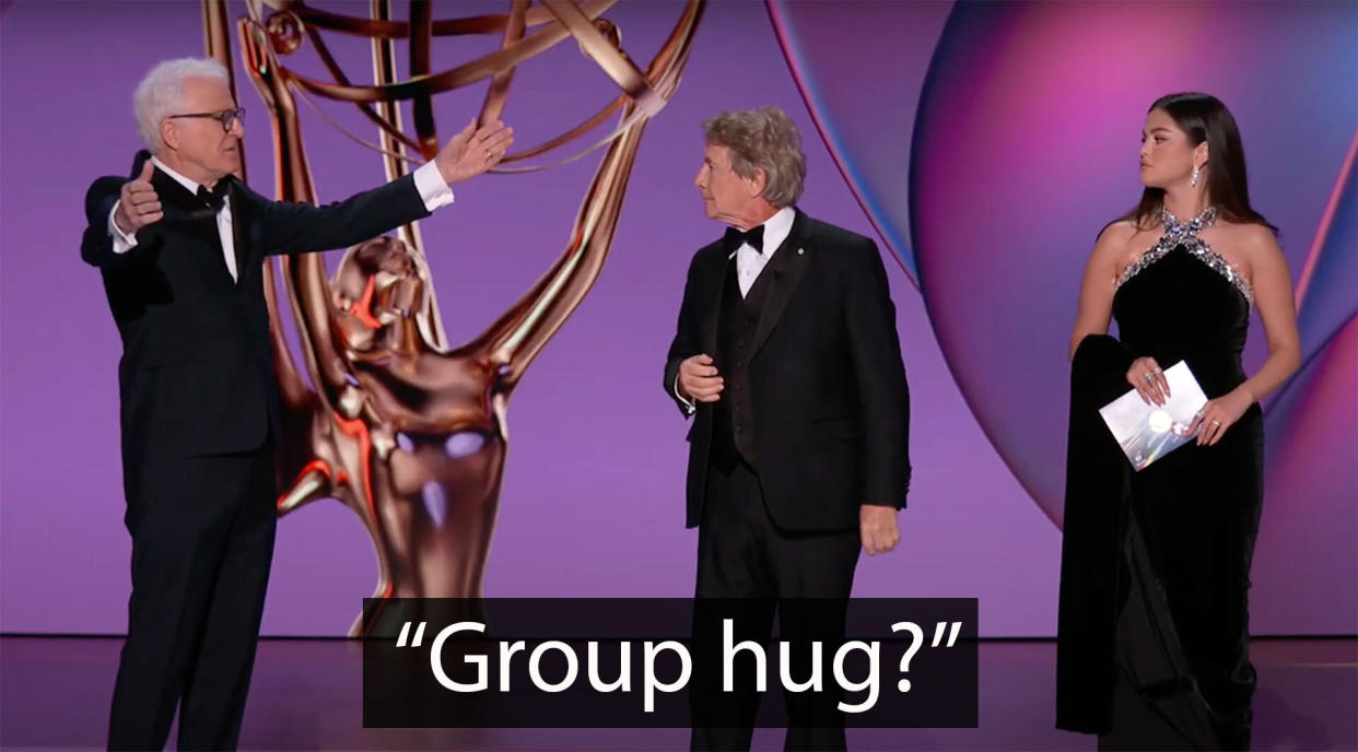 Two men and a woman stand on an awards show stage.