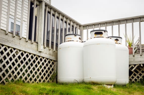 Three propane tanks on a grassy area near the deck alongside a house.