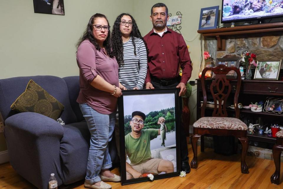 Iris Bonilla, left, lost her son, Jose Bonilla Canaca, in a scaffolding collapse in 2023. Bonilla, her daughter Amy, and her husband Osman Reyes stand with a photo of Jose holding the first fish he’d caught. “Every day, there is a pain in my heart,” Iris said.