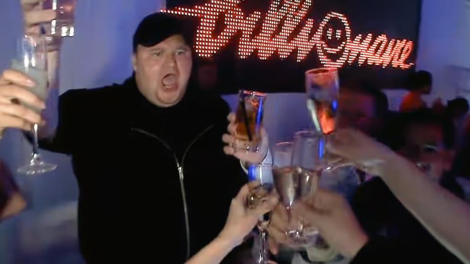 Kim Dotcom partying, toasting glasses with various others in a club atmosphere. Still from music video.