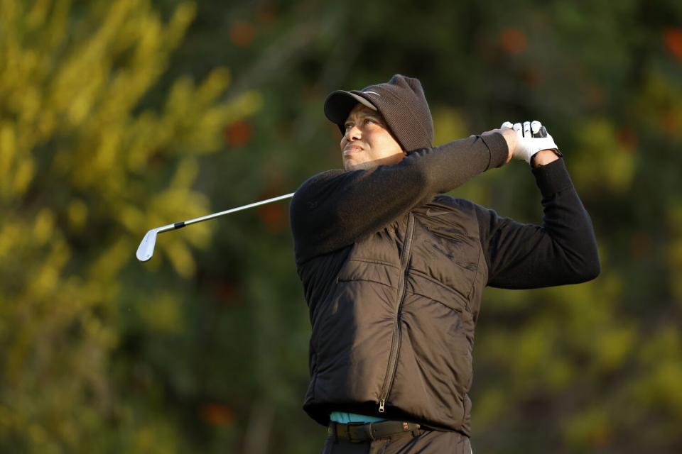Tiger Woods, bundled against the chill, follows through on a tee shot
