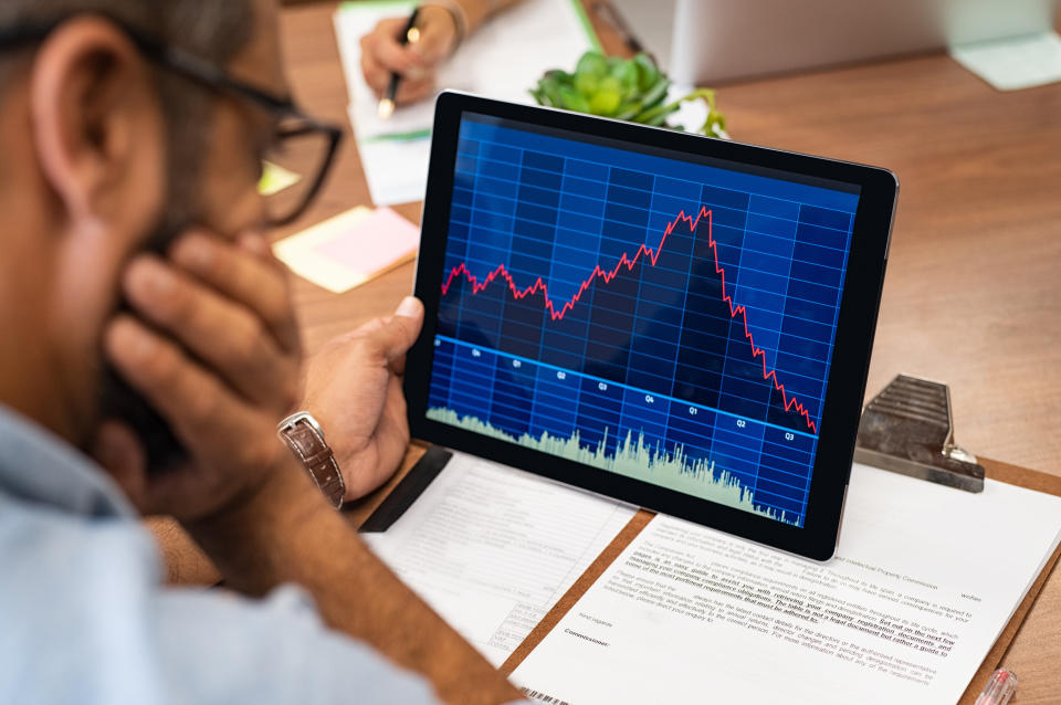 Closeup of a stock market broker working with graphs on digital tablet at office. Rear view of stock agent reading bad report and graph. Back view of multiethnic businessman analyzing fall sales.