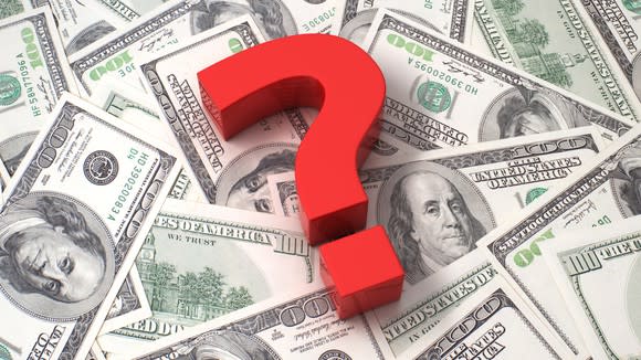 A red question mark on top of a pile of $100 bills
