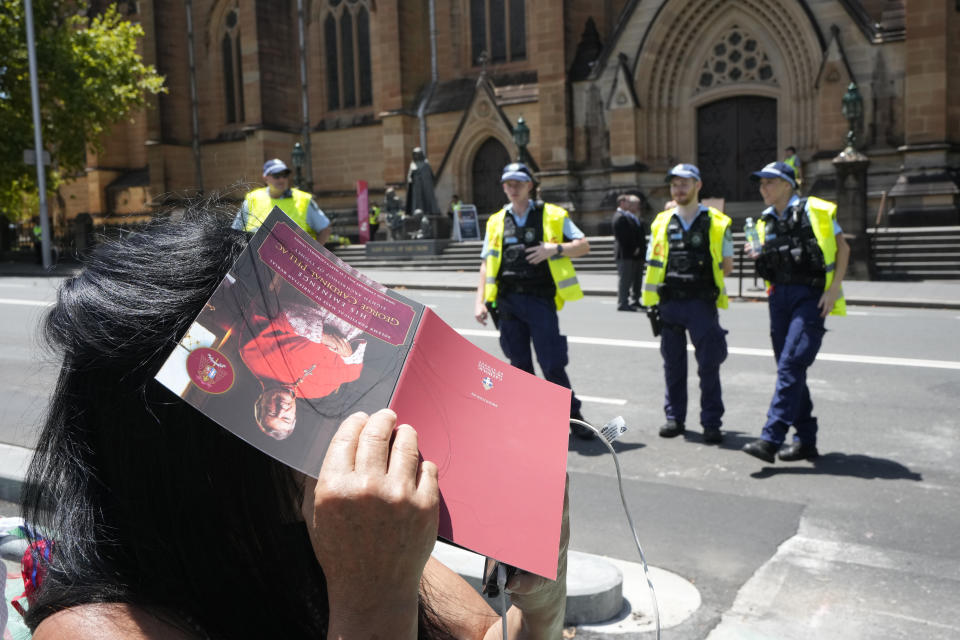 A woman uses a program to block the sun as she uses her phone to live stream the funeral of Cardinal George Pell as police guard St. Mary's Cathedral in Sydney, Thursday, Feb. 2, 2023. Pell, who died last month at age 81, spent more than a year in prison before his sex abuse convictions were overturned in 2020. (AP Photo/Rick Rycroft)