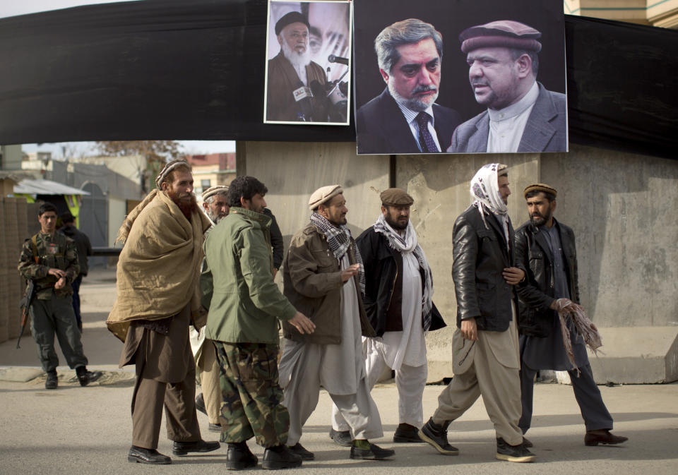 Afghan men cross a street next to a blast wall decorated with pictures of Afghan politicians late Burhanuddin Rabbani, Afghan presidential candidate Abdullah Abdullah and late Afghan Vice President Mohammed Qasim Fahim, from left to right, in the center of Kabul, Afghanistan, Monday, March 10, 2014. Afghanistan's influential Vice President Fahim, a leading commander in the alliance that fought the Taliban who was later accused with other warlords of targeting civilian areas during the country's civil war, died March 9, 2014. He was 57. (AP Photo/Anja Niedringhaus)