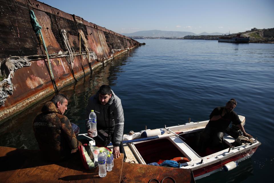 A diver takes a break as a delivery boy brings coffee and water to the crew during a shipwreck raising operation, on Salamina island, west of Athens, on Thursday, Jan. 31, 2020. Greece this year is commemorating one of the greatest naval battles in ancient history at Salamis, where the invading Persian navy suffered a heavy defeat 2,500 years ago. But before the celebrations can start in earnest, authorities and private donors are leaning into a massive decluttering operation. They are clearing the coastline of dozens of sunken and partially sunken cargo ships, sailboats and other abandoned vessels. (AP Photo/Thanassis Stavrakis)