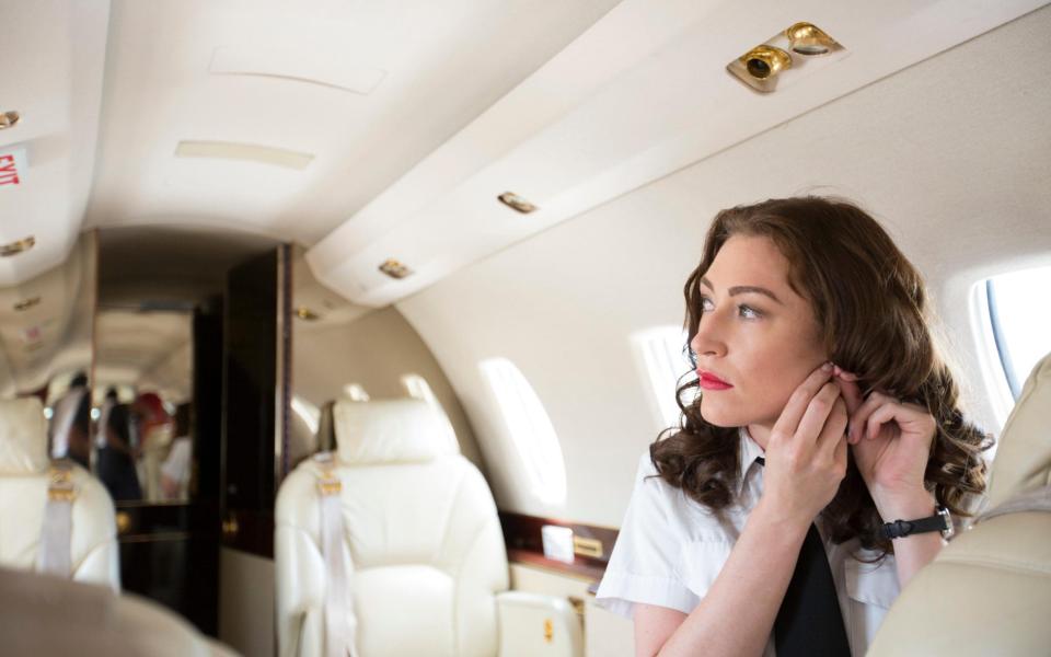 Female flight attendant putting on earring in cabin of private jet - Alamy Stock Photo