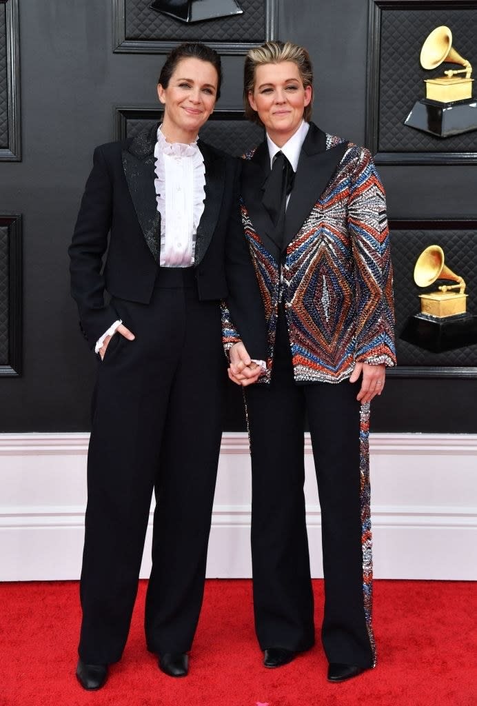 Catherine in a pantsuit with a ruffled shirt and Brandi, also in a pantsuit with a colorful jacket, holding hands