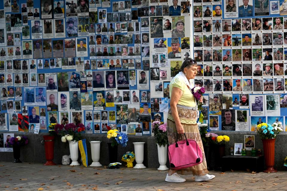 An elderly woman carries flowers past new pictures on the Memory Wall of Fallen defenders of Ukraine in Kyiv on Sept. 27, 2023.