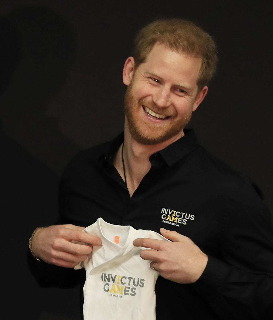 Britain's Prince Harry holds an outfit for his newborn son presented by Princess Margriet of the Netherlands at the launch of the 2020 Invictus Games, in The Hague, Netherlands, Thursday, May 9, 2019. Prince Harry returned to his royal duties Thursday after the birth of his son Archie Harrison, to launch the countdown for the fifth Invictus Games sports competition for injured service personnel and veterans. (AP Photo/Peter Dejong)